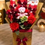 Valentine gift box Lahore with red flowers, pink teddy bear, and greeting card