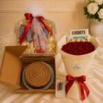 Fresh red rose bouquet next to a chocolate cake and gift box for people who send flowers and cakes