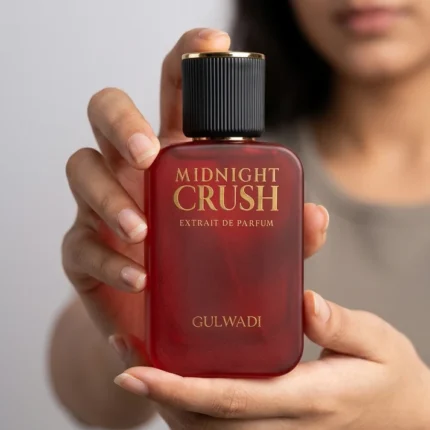 Hands holding a red frosted bottle of Midnight Crush Extrait de Parfum by Gulwadi with gold lettering