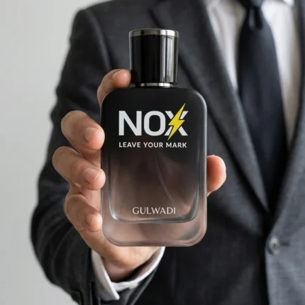 A man in a sharp grey suit holding a bottle of NOX Perfume by Gulwadi featuring white pepper, bergamot, and tonka bean