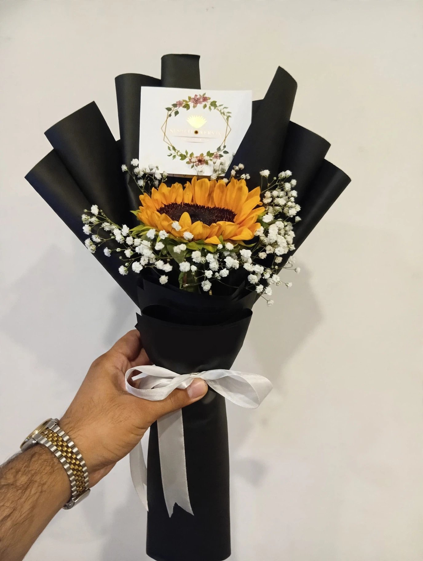 Single fresh sunflower with baby's breath in black wrapping with white ribbon and message card